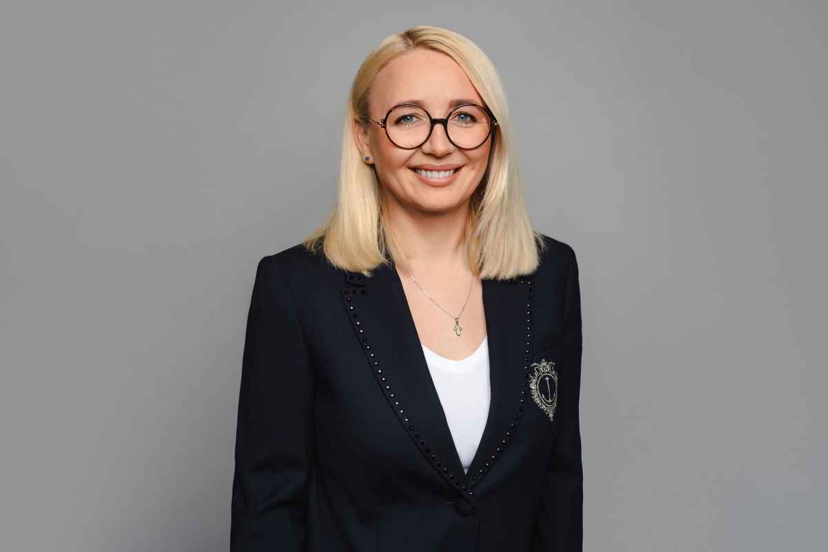 Jauna moteris su ilgesniais šviesiais plaukais dėvi juodus akinius ir tamsią švarką.